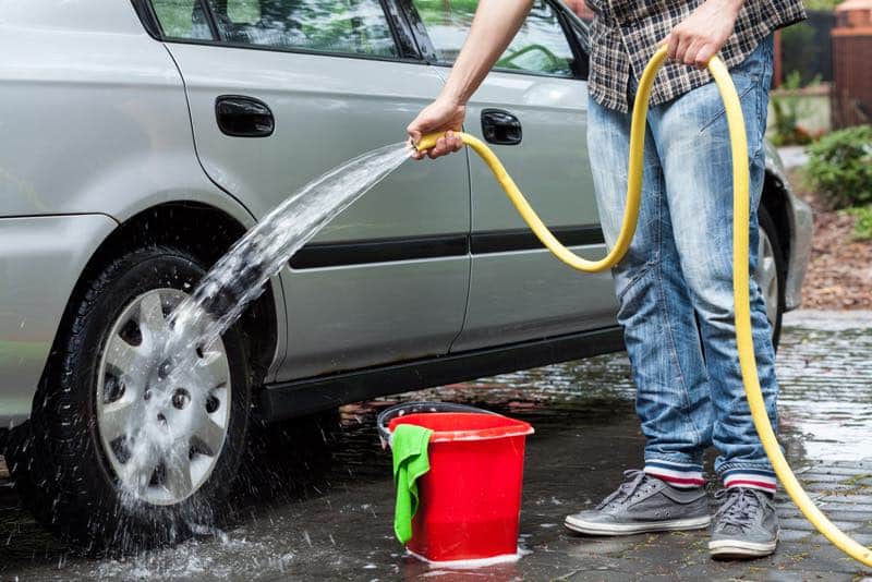 Man wäscht sein Auto mit einem Wasserschlauch